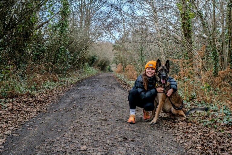 Smiling woman with German Shepherd on a forest path in autumn.